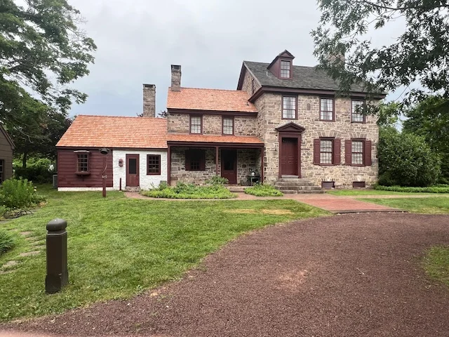 Historic stone house with a red roof and wooden shutters, surrounded by green lawn and trees, representing traditional architecture in Pipersville, PA.