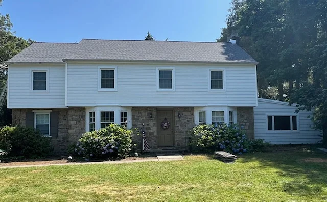 Two-story home featuring white vinyl siding, stone accents, and landscaped front yard with flowering shrubs, illustrating professional siding installation by Franco Roofing, Inc. in Bucks County, PA.