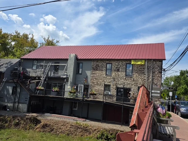 Franco Roofing installation showcasing a stone building with a red metal roof in Newtown, Pennsylvania, emphasizing local expertise and quality materials.