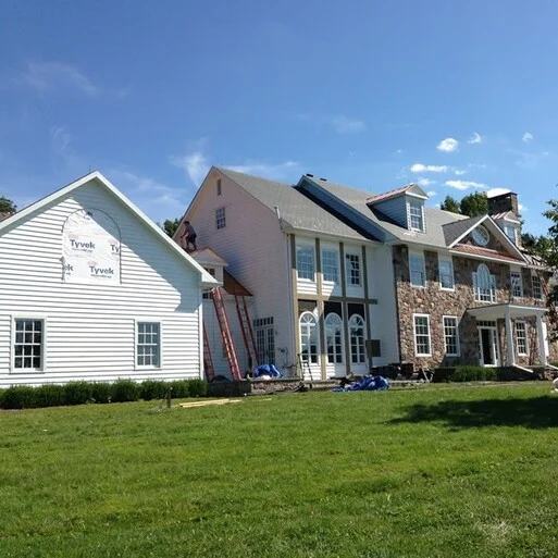 Vinyl siding installation on a residential home in Montgomery County, showcasing Tyvek moisture barrier, professional tools, and ongoing work by Franco Roofing, emphasizing quality siding services.